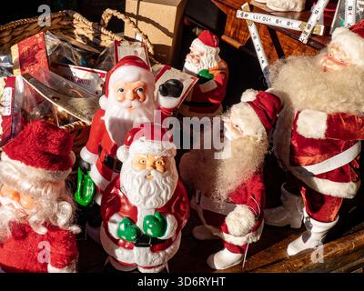 Un groupe de figurines de père Noël vintage dans la lumière chaude de l'après-midi, rouges festifs et barbes moelleuses envahissant un étalage de vacances. Banque D'Images