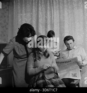 Slaviansk, région de Donetsk, RSS d'Ukraine, Union soviétique. Février 1986. La famille du député Kolesnik passant une soirée à la maison. Le père lit le journal de la Pravda tandis que la mère regarde leur fille aînée tricoter avec de la laine. La jeune fille se tient derrière la lecture d'un livre. Ils portent des vêtements décontractés dans une pièce avec des rideaux à motifs. Cette photographie d'archives en noir et blanc capture une scène de loisirs domestiques traditionnels dans la paisible région du Donbass bien avant la guerre. Banque D'Images