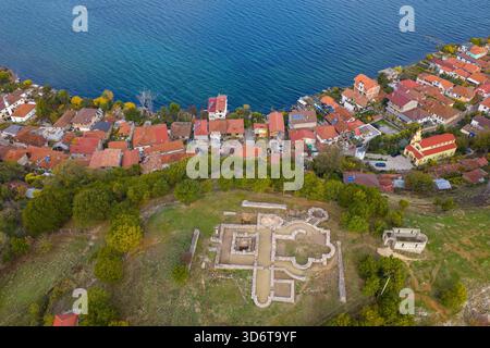 Vue aérienne des ruines de la basilique antique de Lin surplombant le village au bord du lac, les toits en terre cuite et les eaux bleues profondes du lac Ohrid. Banque D'Images