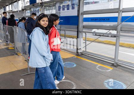 Les passagers font la queue sur une plate-forme couverte à une station de transport rapide de bus urbains à Lima, au Pérou. Les garde-corps métalliques, les marquages au sol et les panneaux s'organisent Banque D'Images