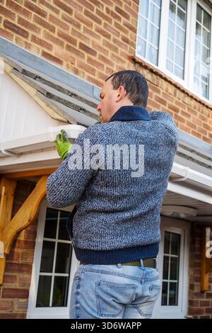 Homme sur une échelle nettoyant les feuilles d'automne tombées et la mousse de la gouttière du toit de la maison. Entretien de la maison, nettoyage des gouttières Banque D'Images