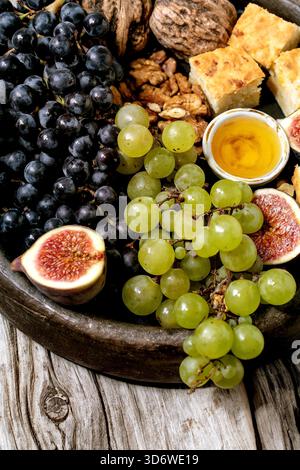 Hors-d'œuvre au vin avec différents raisins, figues, noix, pain, miel et fromage de chèvre sur plaque de céramique sur fond de bois ancien. Gros plan Banque D'Images