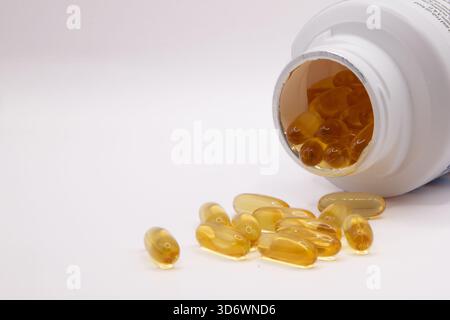 Comprimés d'huile de foie de morue se déversant d'un récipient ouvert sur un fond blanc propre, idéal pour la santé et les thèmes des suppléments. Banque D'Images