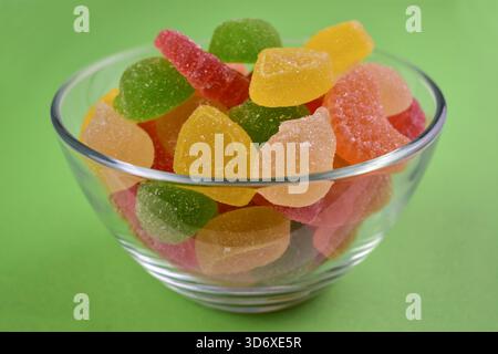 Bonbons à la gelée, marmelade dans un bol transparent sur fond vert. Gros plan. Banque D'Images