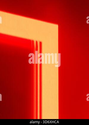 Surface murale rouge avec une tache rectangulaire de lumière et des ombres verticales formant une composition géométrique abstraite et minimaliste de lignes, de texture et de vi Banque D'Images