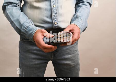 Gros plan de l'homme ouvrant le portefeuille plein de billets de banque, représentant la finance personnelle, l'économie de trésorerie d'épargne. Les mains masculines comptent l'argent à l'intérieur du portefeuille en cuir, c Banque D'Images