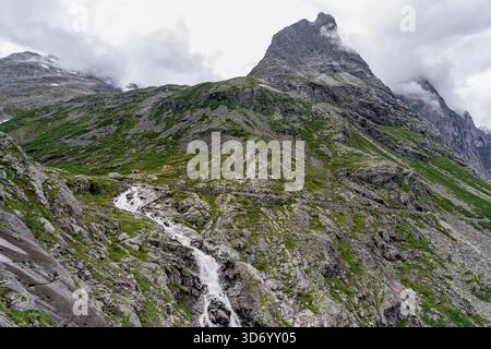 Maisons isolées à pied des tours de montagne Bispen au-dessus du paysage rocheux, avec la cascade Stigfossen descendant ses pentes rocheuses en Norvège Banque D'Images