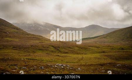 Vallée de montagne irlandaise brumeuse dans le parc national du Connemara en Irlande avec des pentes vallonnées et des nuages bas dérivant à travers les sommets Banque D'Images