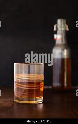 Un verre de roches vintage partiellement rempli d'alcool brun, bouteille en arrière-plan Banque D'Images