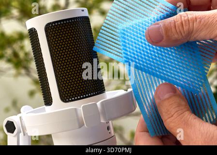 Mains manipulant des couches de maille en plastique bleu près d'un microphone à condensateur blanc pour enregistrer les rayures et les déclenchements audio ASMR texturés. Banque D'Images