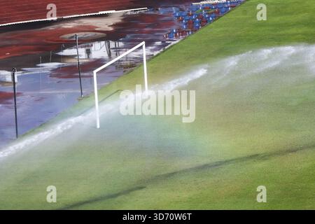Scène rafraîchissante du système d'arrosage arrosant le terrain de football vert. le jet d'eau crée un bel arc-en-ciel sur un gazon luxuriant à côté d'un poteau de but blanc dans sta Banque D'Images