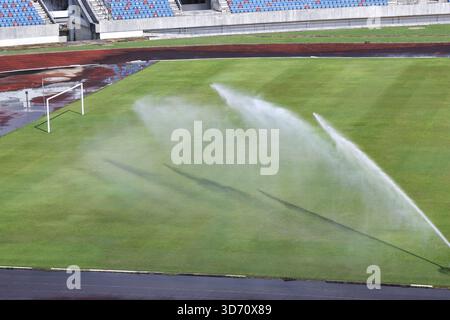 Arrosage d'un terrain de football en herbe verte avec système d'arrosage dans un stade vide. Entretien du gazon et du terrain avant compétition sportive, vue des refres Banque D'Images