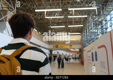 Une personne avec un sac à dos se tient dans un terminal d'aéroport occupé, prêt à voler. Aéroport de Calgary Banque D'Images