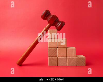 L'image montre un marteau en bois à côté d'une pile de cubes en bois sur un fond rouge. Banque D'Images