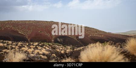 Paysage de vallée de montagne volcanique avec des pentes rouges végétation sèche et ciel nuageux lumineux Banque D'Images