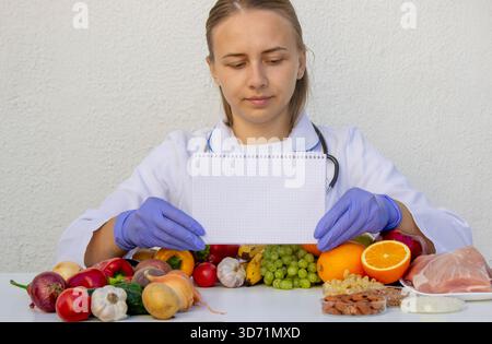 Nutritionniste tenant un bloc-notes vierge pour écrire un plan de régime parmi les fruits et légumes. Banque D'Images