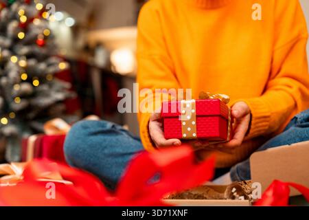 Femme portant un pull jaune tenant une boîte cadeau de Noël de couleur rouge dans ses mains. Banque D'Images