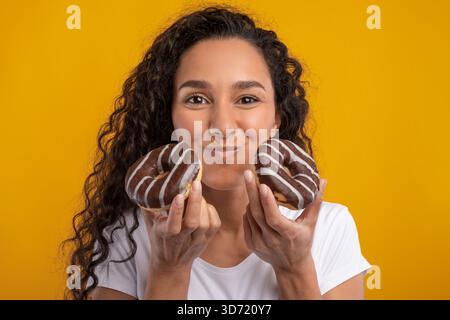 Funny Latin Lady apprécie Donuts et exprime sa joie dans un cadre Studio dynamique Banque D'Images