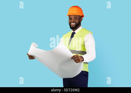 Un entrepreneur afro-américain souriant tient des bleus tout en se tenant isolé sur fond bleu Banque D'Images