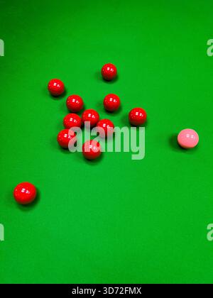 Une vue rapprochée et en grand angle de plusieurs boules de snooker rouges et une boule rose dispersées sur le feutre vert vif d'une table de billard. Banque D'Images