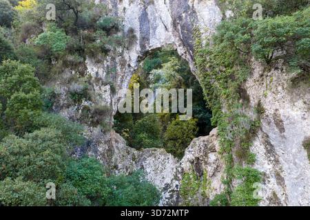 Fenêtre en arc de roche naturelle encadrant une cascade dans la distance cachée dans un canyon forestier vert à Corfou Grèce drone aérien prise de vue géologique Banque D'Images