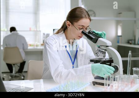 Jeune scientifique femme caucasienne examinant des échantillons à l'aide d'un microscope en laboratoire Banque D'Images