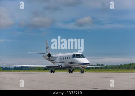 les jet taxis d'affaires traversent la piste sous un large ciel bleu avec des nuages lointains. Capturée à partir d'un angle de quart avant, la composition met en valeur à la fois eng Banque D'Images