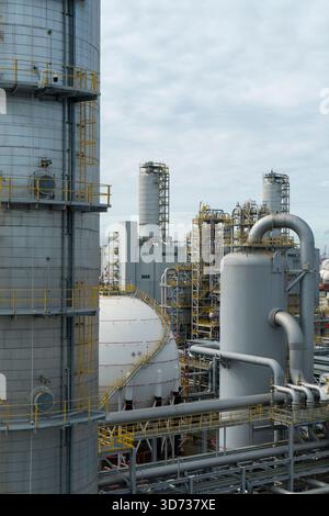 Une vue détaillée d'une installation pétrochimique moderne avec des réservoirs de gaz sphériques, de hautes tours de traitement et des systèmes de tuyauterie complexes sous ciel nuageux. Banque D'Images