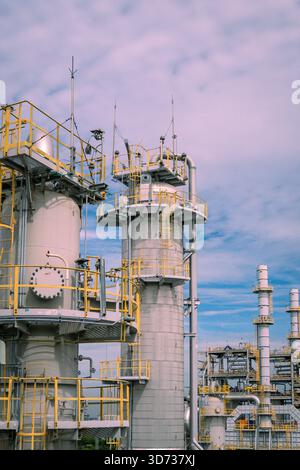 Une vue rapprochée des tours de traitement de raffinerie avec des plates-formes métalliques, des échelles, des systèmes de tuyauterie et des rampes de sécurité industrielle sous un ciel lumineux. Banque D'Images