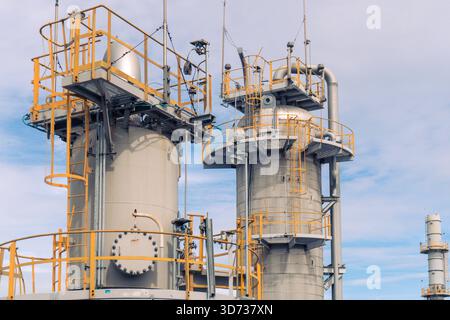 Une vue rapprochée des tours de traitement de raffinerie avec des plates-formes métalliques, des échelles, des systèmes de tuyauterie et des rampes de sécurité industrielle sous un ciel lumineux. Banque D'Images