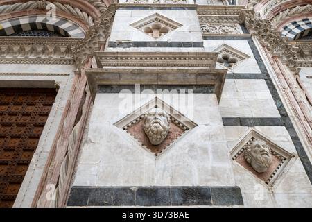 Sienne, Italie - 19 juillet 2025 : façade gothique de la cathédrale de Sienne avec des rayures de marbre blanc et foncé, des têtes sculptées et des arches complexes. Banque D'Images