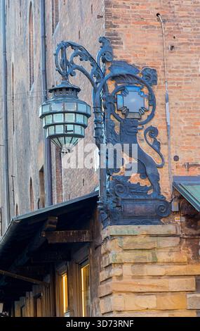 La ferronnerie décorative présente un dragon et une lanterne à côté d'un mur de pierre sur la Piazza Del Nettuno, en Italie. Une lumière chaude met en valeur l'architecture en brique et l'ancienne Banque D'Images