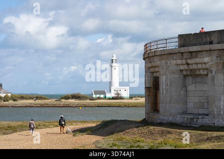 Walker sur Hurst Spit au château de Hurst, une forteresse d'artillerie obsolète, avec le phare de Hurst point et la maison du gardien derrière, en Angleterre Banque D'Images