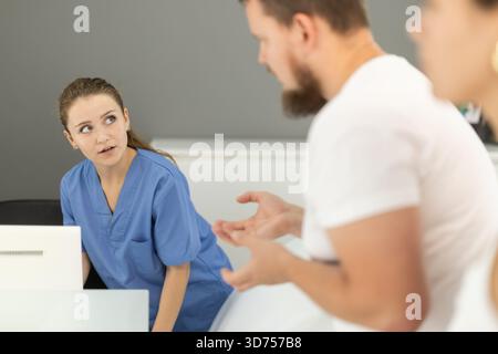 L'homme se tient près de la réception et pose des questions à l'administrateur de la dentisterie Banque D'Images