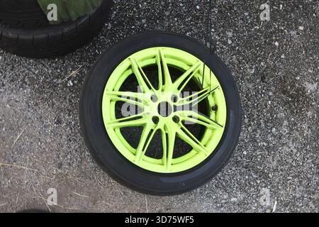 Roue de voiture verte néon vibrante avec pneu noir couché sur fond de béton. la jante en alliage remarquable présente une conception à rayons multiples pour un look automobile personnalisé Banque D'Images