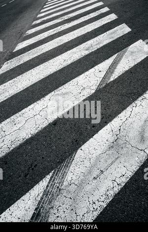 Image verticale d'un passage piéton zèbre usé peint sur une surface de route asphaltée. Mise au point sélective. Banque D'Images