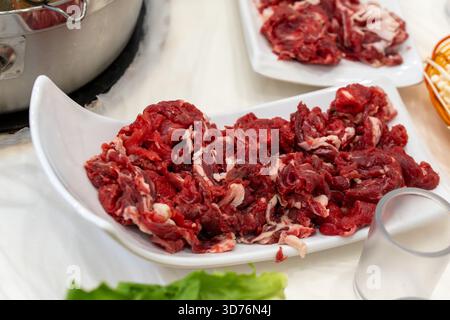 Un gros plan de bœuf cru fraîchement tranché sur une assiette blanche, préparé pour un repas chaud. La viande rouge éclatante met en valeur la fraîcheur, les protéines, et comme Banque D'Images