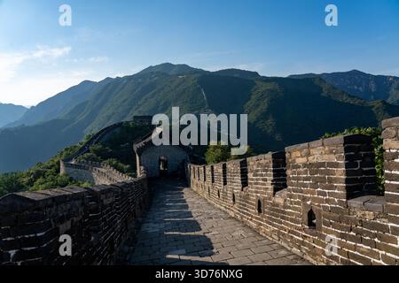 Le sentier de la Grande Muraille passe devant une petite maison de garde en pierre sur une crête de montagne. De longues ombres tombent sur le chemin, soulignant la structure historique et v Banque D'Images