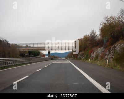 Frioul, Italie 21 novembre 2025 conduite sur l'autostrada européenne vers le passage supérieur, perspective de l'asphalte, marquages routiers, garde-corps et SK d'automne nuageux Banque D'Images