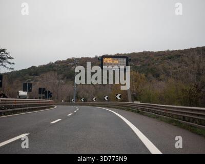 Frioul, Italie 21 novembre 2025 autoroute italienne sinueuse à travers le paysage d'automne avec panneau de route électronique lisant LAVORI ATTENZIONE, vide, terminé Banque D'Images