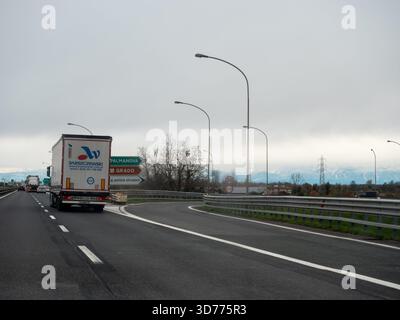 Frioul, Italie 21 novembre 2025 camion roulant sur une autoroute italienne vers une sortie, avec des panneaux pour Palmanova et Grado, montagnes dans le distan Banque D'Images