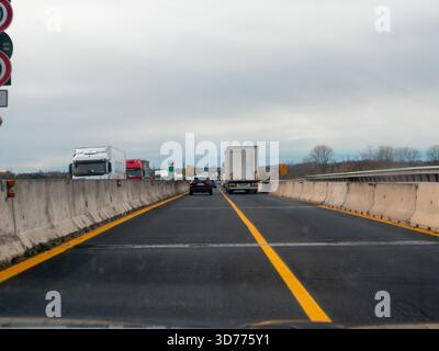 Frioul, Italie 21 novembre 2025 véhicules et camions se déplaçant le long d'une autoroute couverte, mouvement flou transportant le voyage, le transport et le flux de banlieue vers Banque D'Images
