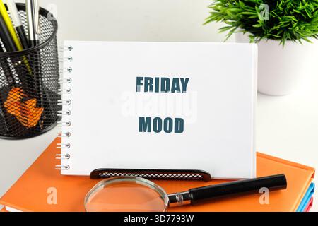 Un bloc-notes sur le dessus des livres affiche les mots Friday Mood. Une loupe, un porte-stylo et une petite plante ornent le bureau, capturant un vendredi Banque D'Images