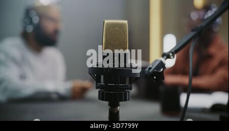 Gros plan du microphone à condensateur professionnel, fournit la technologie audio, un son de haute qualité. Deux hommes brouillaient en arrière-plan, réalisant un podcast ou une interview. Échange créatif dans l'espace médiatique moderne. Banque D'Images