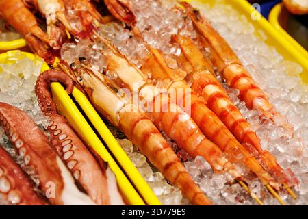 Gros plan de grosses crevettes et de tentacules de poulpe disposés sur de la glace pilée dans une exposition de marché. L'image montre des couleurs vives et de la fraîcheur. Banque D'Images