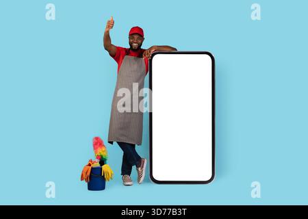 Black Cleaner Homme debout près de Big Blank smartphone et montrant Thumb Up Banque D'Images