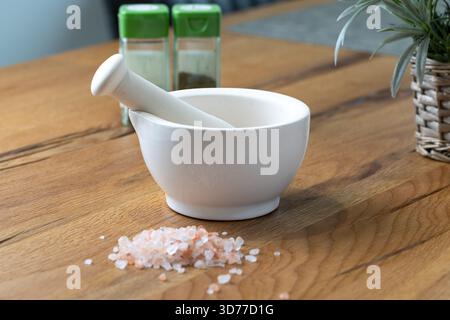 Pilon et mortier avec du sel rose de l'Himalaya et des pots d'épices sur une table rustique en chêne dans une lumière naturelle douce. Banque D'Images