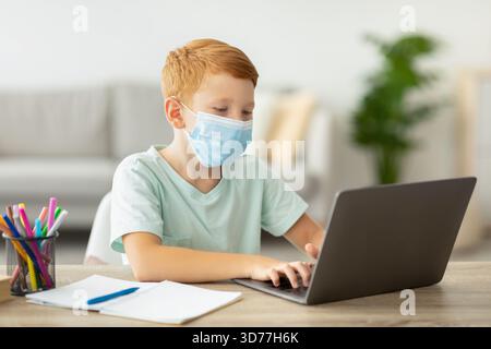 Redhead Boy in a Mask apprendre à la maison à l'aide d'un ordinateur portable pendant la pandémie Banque D'Images