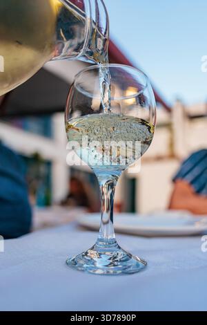 Verser du vin blanc dans le verre à la table du restaurant en plein air Banque D'Images