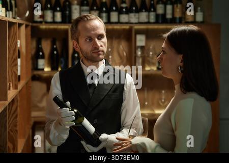 Caucasien jeune homme adulte présentant une bouteille de vin à la femme caucasienne dans la cave Banque D'Images